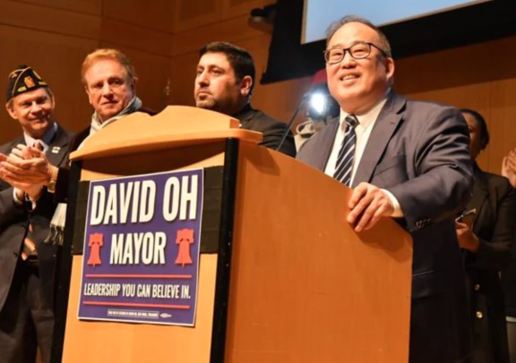 David Oh stands at a podium with his campaign sign