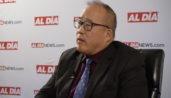 David Oh sitting in a black chair in front of an Al Día banner