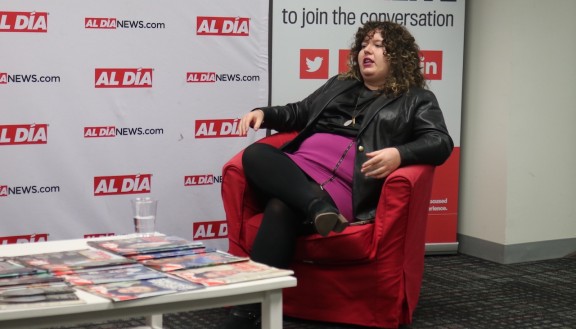 Amanda McIllmurray sitting in a red chair in front of an Al DÍA banner 