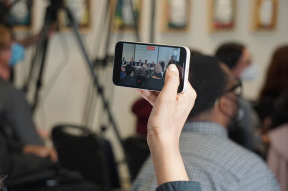 a hand holding up a phone that is recording a mayoral forum on disability issues