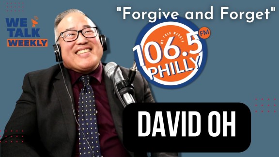 David Oh with headphones on sitting behind a radio mic