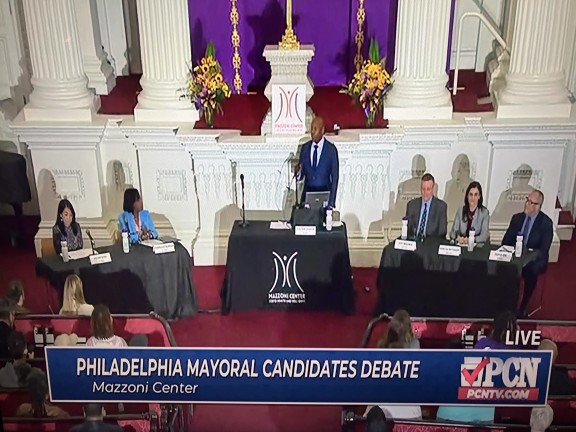 Candidates sitting behind tables in front of an audience at a forum