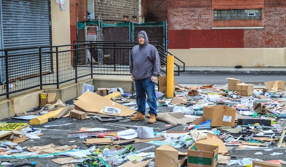 Man in gray hoodie standing among trash