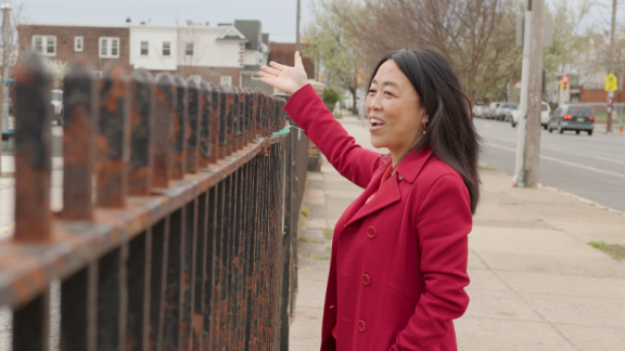 Helen Gym smiling while looking over a rusted fence