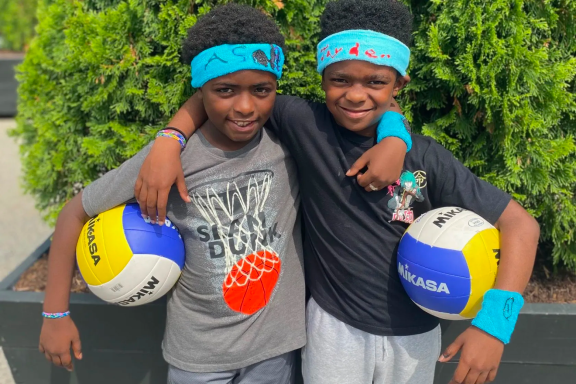 Two young kids embracing and holding volleyballs