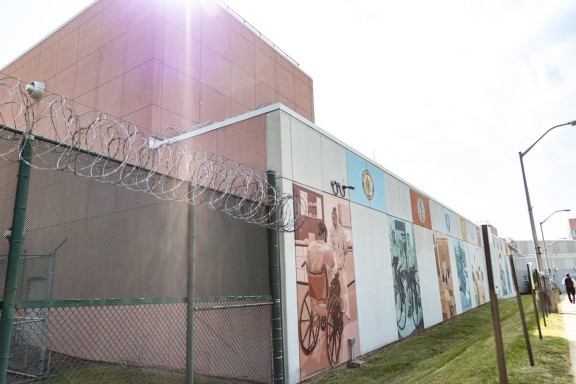 Correctional facility wall with mural next to a gate topped with barbed wire