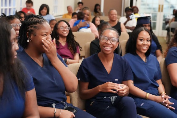 Women dressed in dark blue scrubs celebrating their graduation