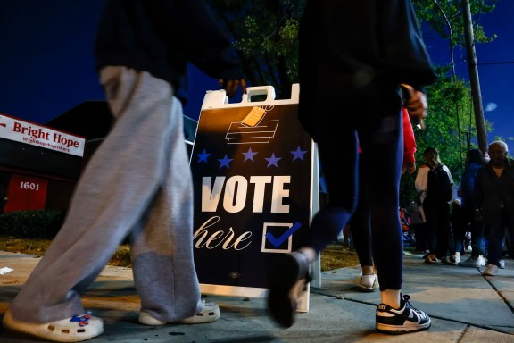 People lining up to vote near a sign saying Vote Here