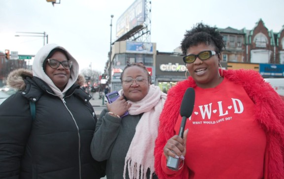 Interviewer Tata Cherise speaking into a mic next to two North Philly residents on the street