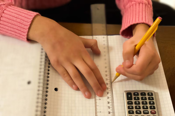 Image of a child's hand holding a pencil and a ruler