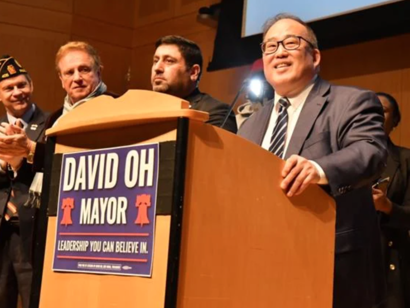 David Oh stands at a podium with his campaign sign