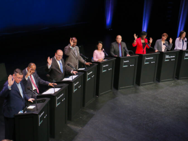 Candidates for mayor of Philadelphia raise their hands behind podiums