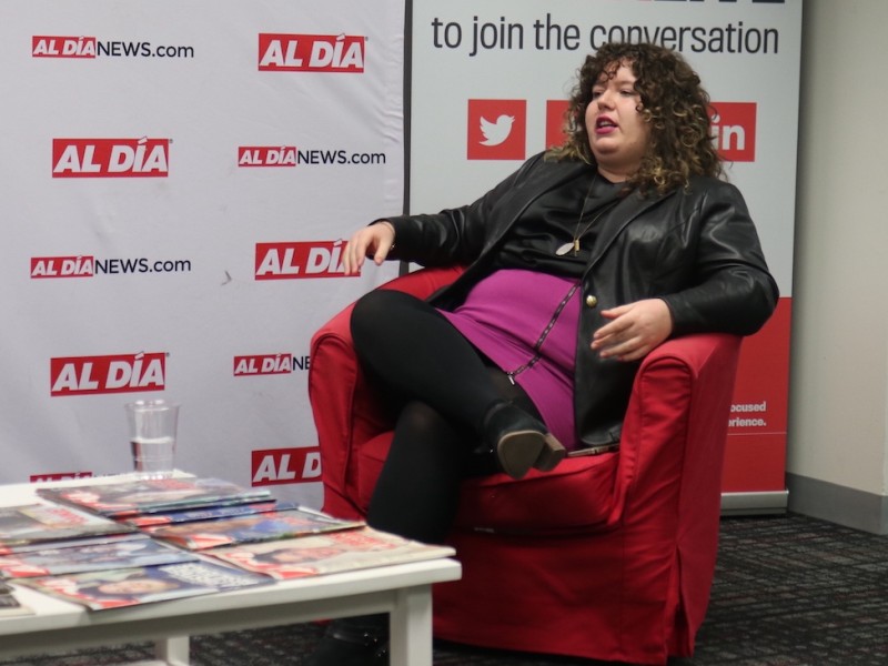 Amanda McIllmurray sitting in a red chair in front of an Al DÍA banner 