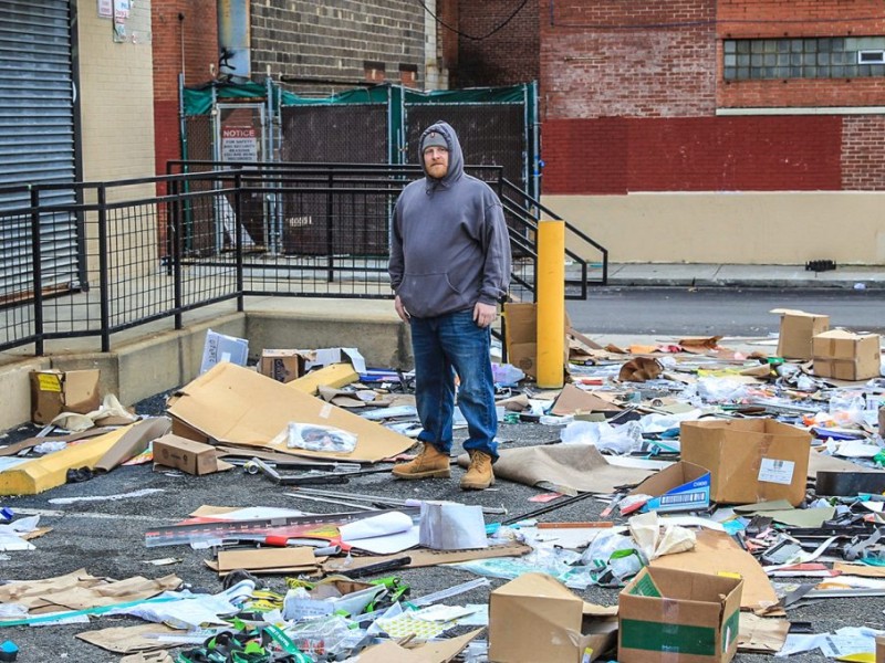 Man in gray hoodie standing among trash 