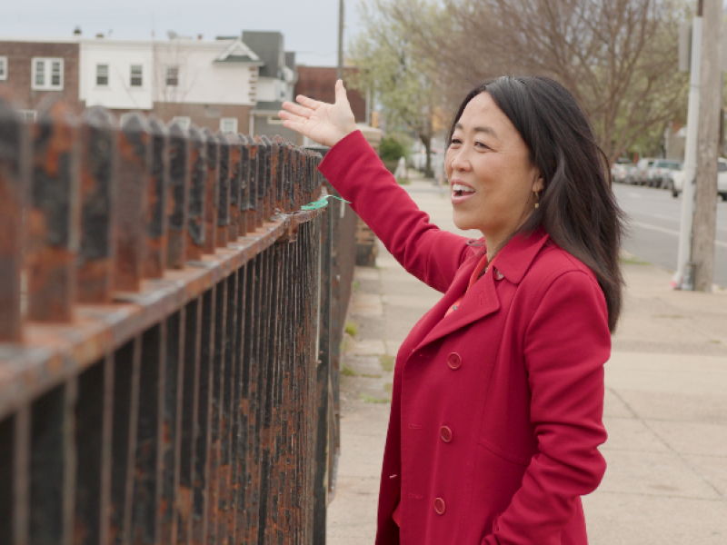 Helen Gym smiling while looking over a rusted fence