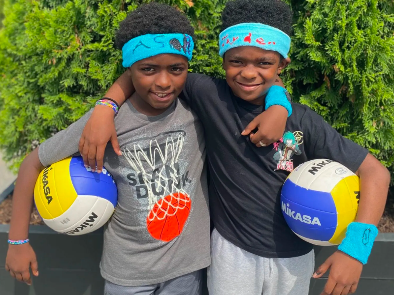 Two young kids embracing and holding volleyballs