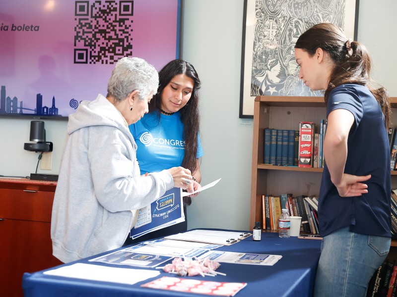 Three people standing around a table full of voter education resources