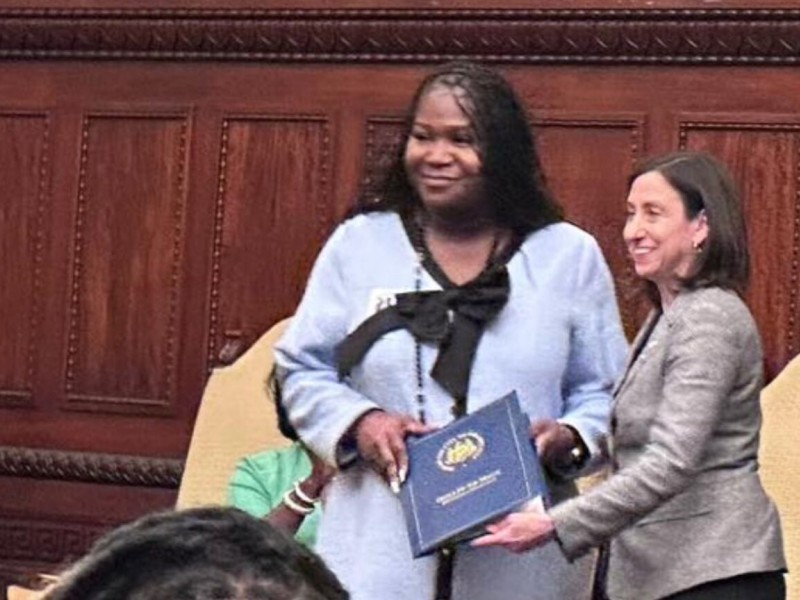 Tatyana Woodard being handed a blue binder by Councilmember Rue Landau during a ceremony that honors her participation on the Philadelphia Commission for Women.