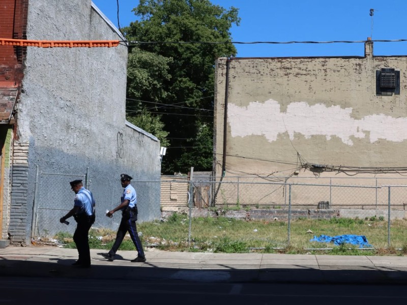 Two police officers walk past empty lot in Kensington neighborhood