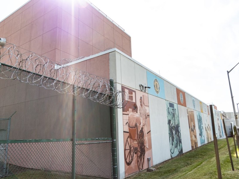 Correctional facility wall with mural next to a gate topped with barbed wire
