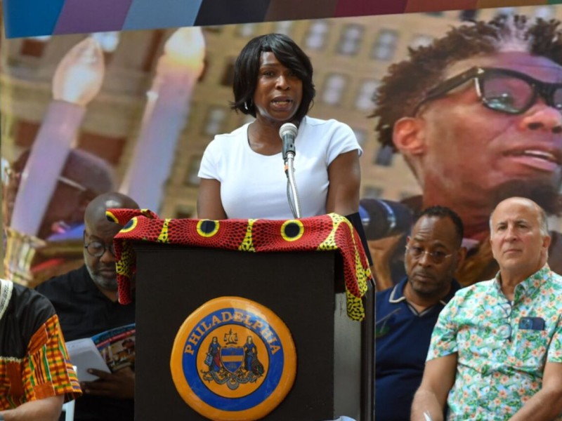 Celena Morrison-McLean speaking in front of a podium during a street dedication for Michael Hinson, Jr.